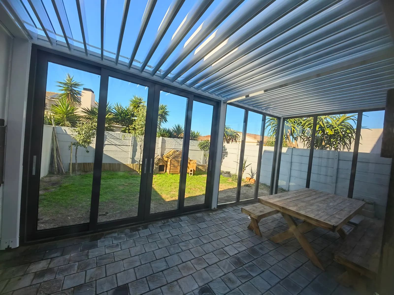 Daylight view under the louvred roof towards the garden through glass sliding doors