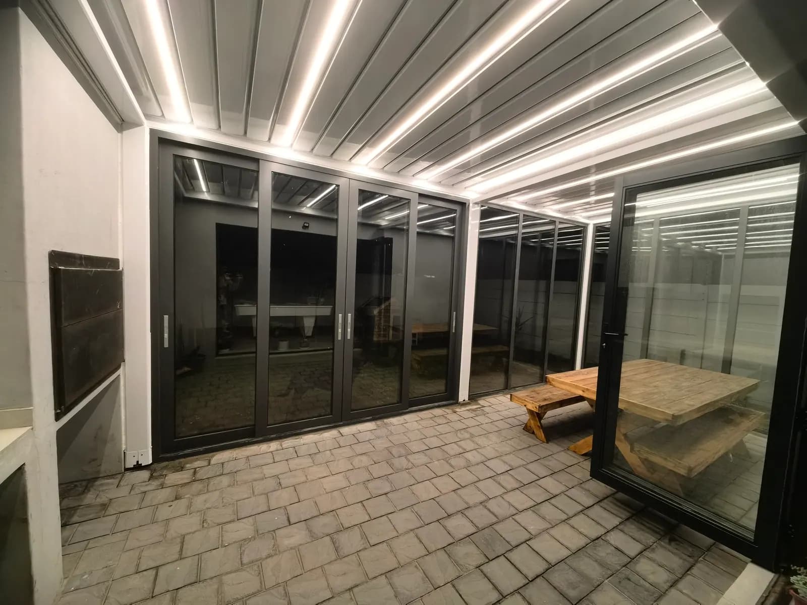 Wide view of the lit pergola interior at night with paving and a bench