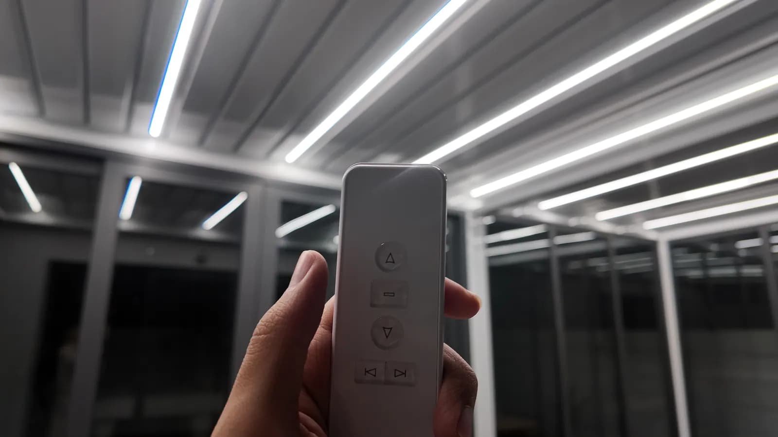 A hand holding the white remote control under the lit louvres