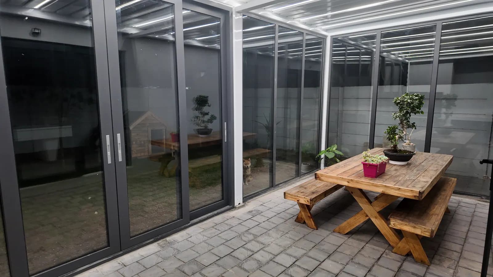 Enclosed louvred roof at night, LED strips glowing above a wooden table, glass sliding doors on two sides