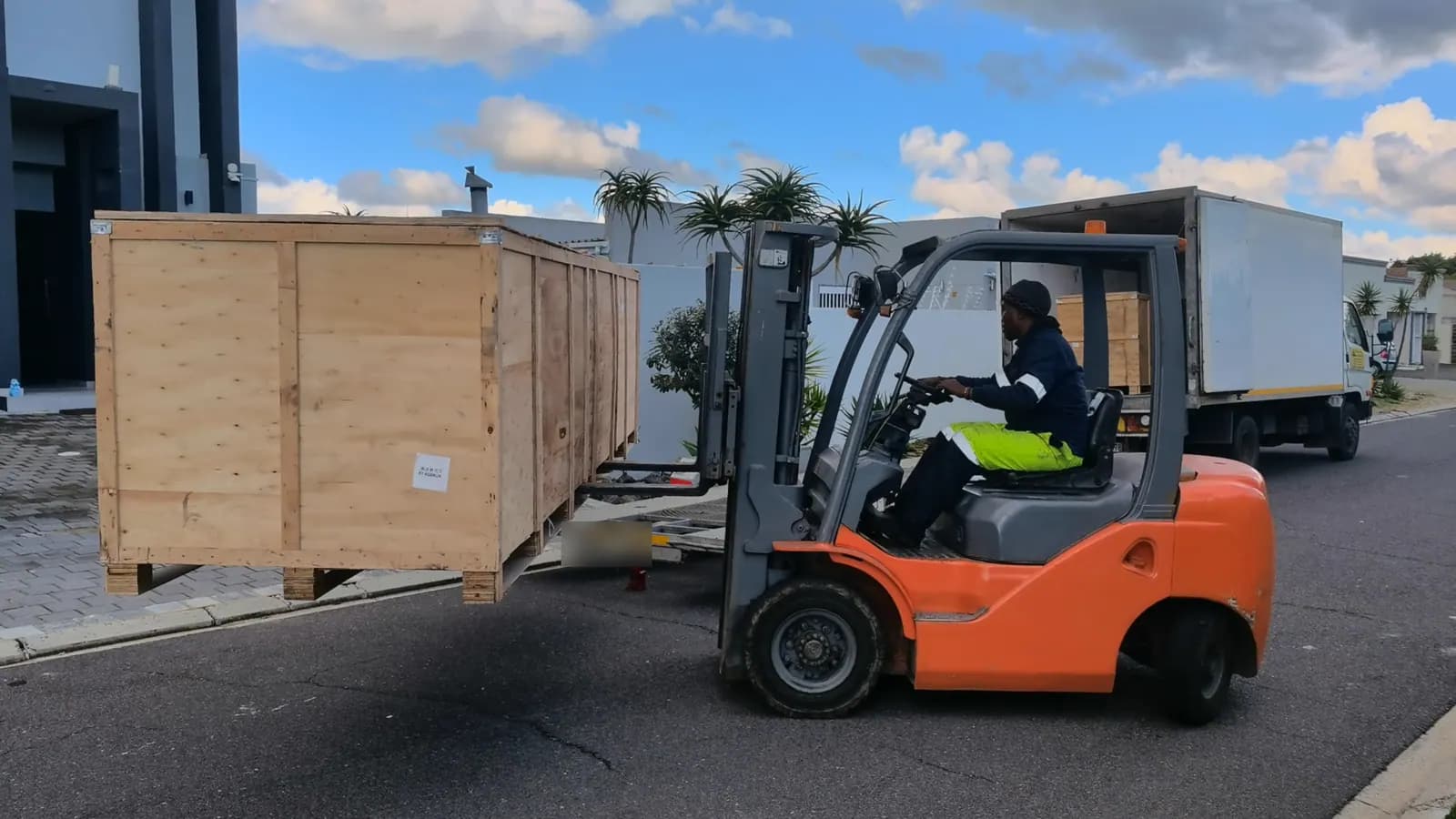 A forklift carrying a wooden export crate of pergola parts from a truck on a Cape Town street