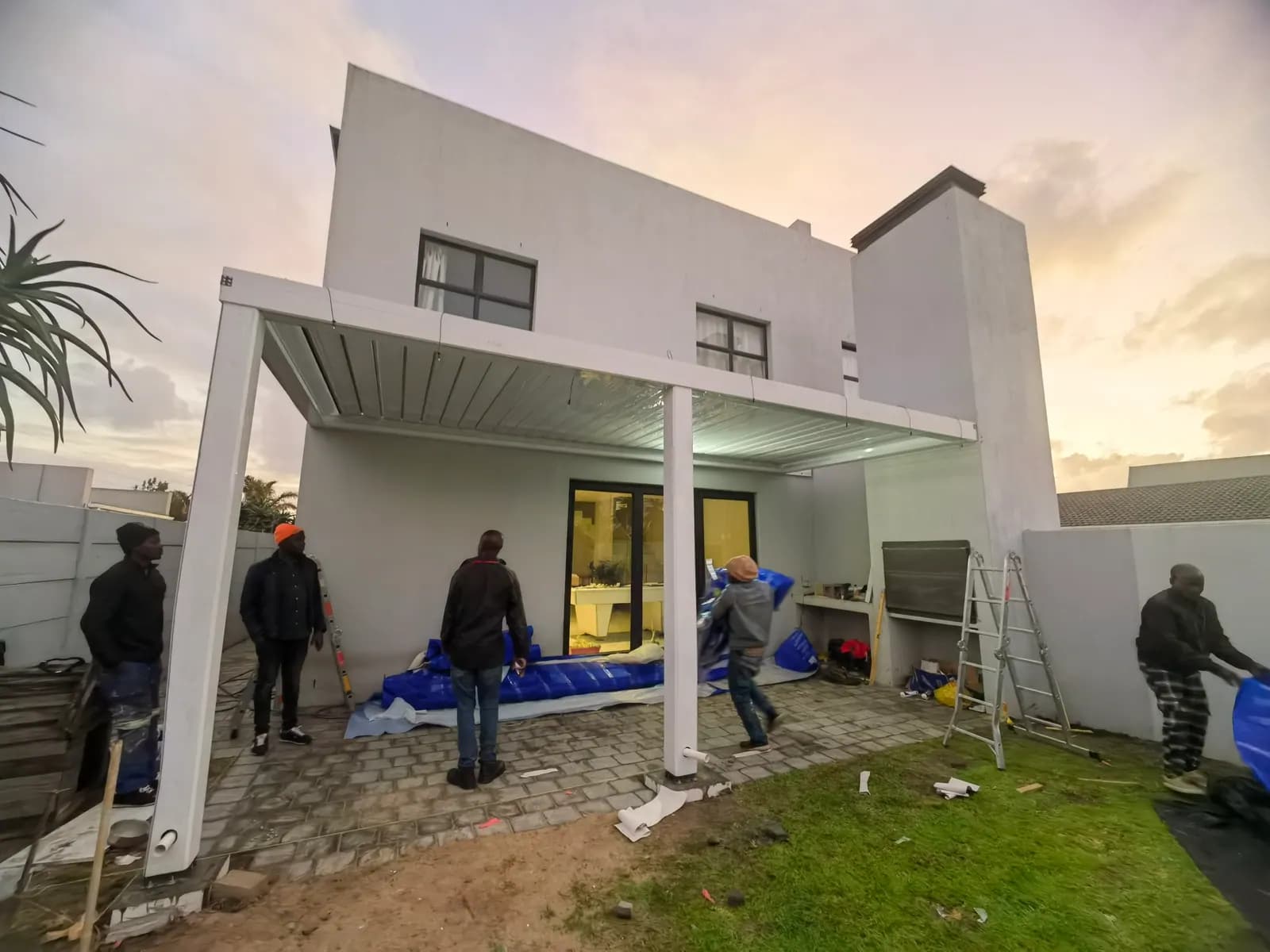 The epergola installation crew standing under a newly raised white pergola frame at sunset
